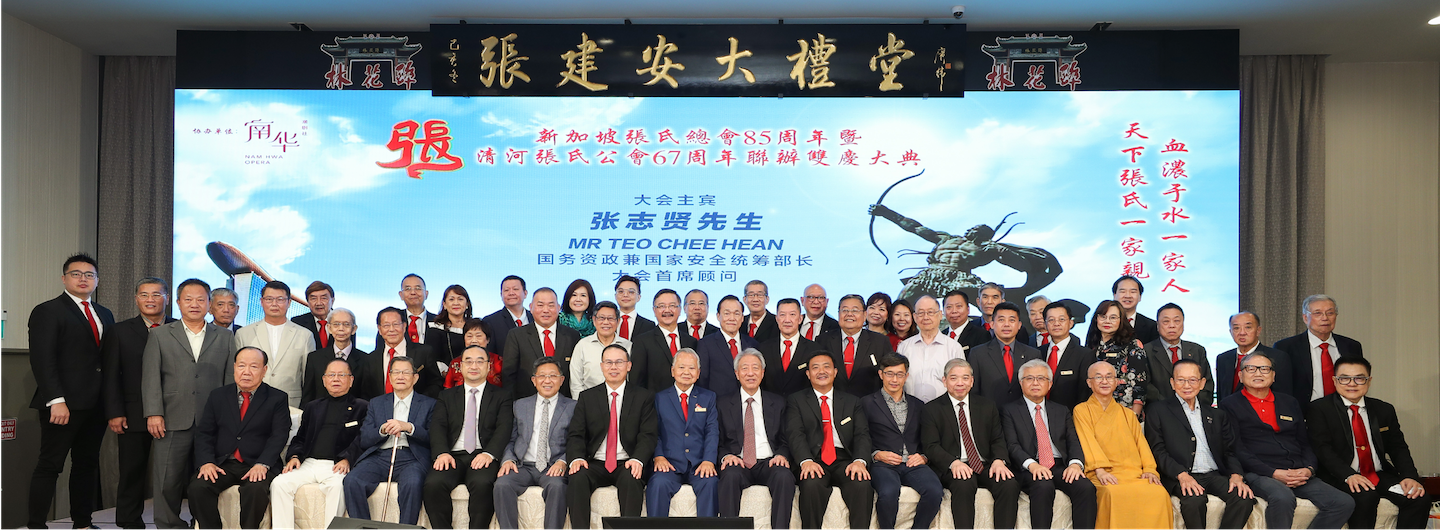 Group of people pose in front of a screen with text and archer statue. Most wearing suits.